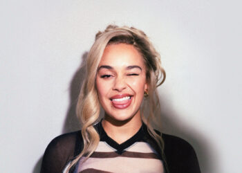 A photo of British singer Jorja Smith smiling in front of a blank wall