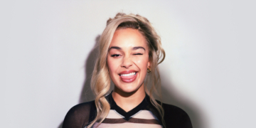 A photo of British singer Jorja Smith smiling in front of a blank wall