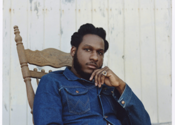 A photo of singer Leon Bridges, wearing a blue denim jacket, sitting in a rocking chair