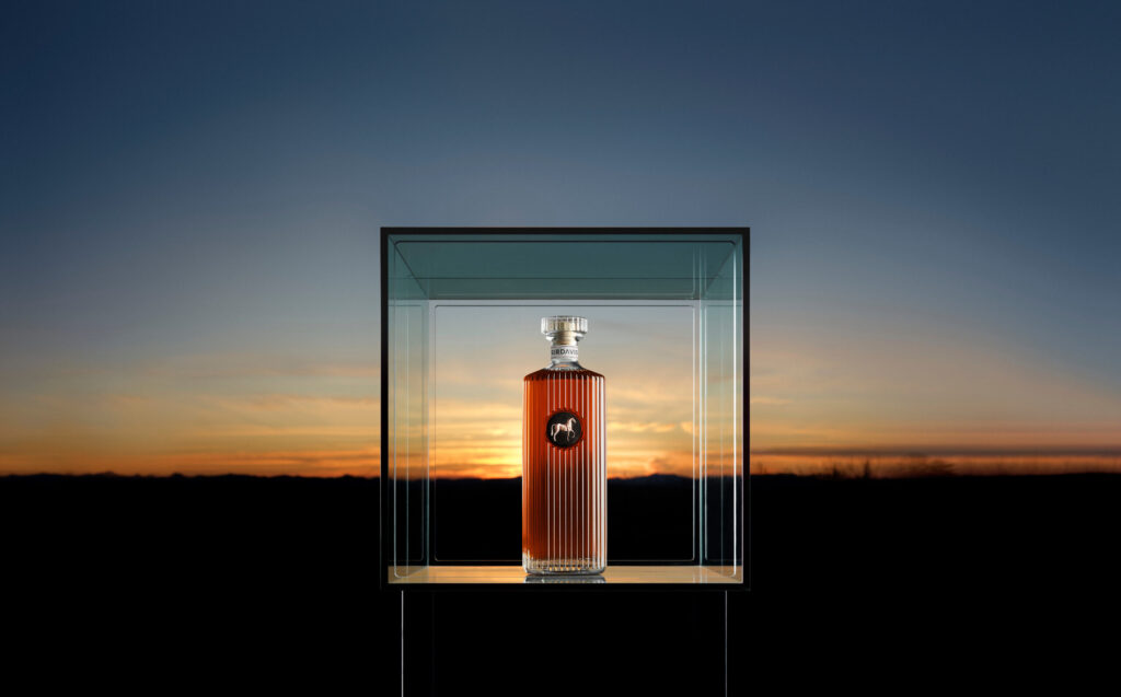 A bottle of Beyoncé's SirDavis whisky encased in a transparent display box, set against a sunset background