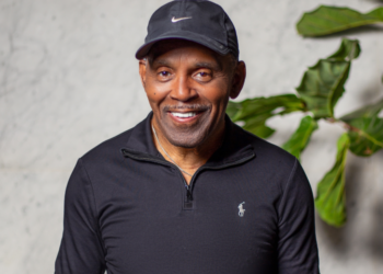 A photo of Frankie Beverly standing in front of a wall with a green plant