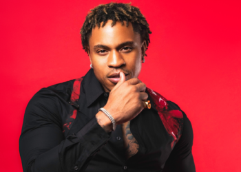 A photo of R&B singer and actor Rotimi in front of a red backdrop
