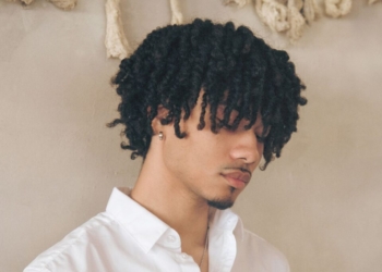 An image of singer Bryant Barnes: standing in front of a tan background, looking down with a white shirt
