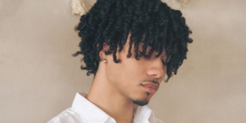 An image of singer Bryant Barnes: standing in front of a tan background, looking down with a white shirt