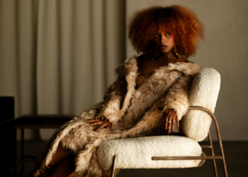 An image of singer Fana Hues sitting on a chair, wearing a fur coat