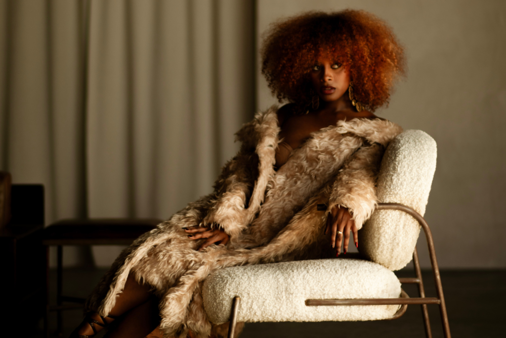 An image of singer Fana Hues sitting on a chair, wearing a fur coat