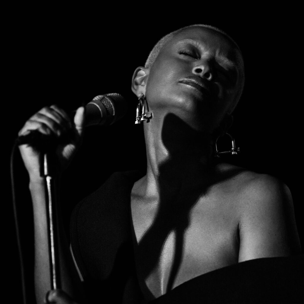 A black and white photo of singer Kela standing on stage with a mic.