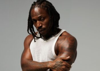 R&B singer SiR poses against a grey backdrop in a white tank top.
