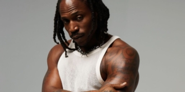 R&B singer SiR poses against a grey backdrop in a white tank top.