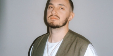 A photo of singer Joe Leone standing in front of a gray wall