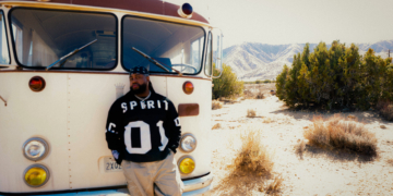 A photo of Xavier Omar standing in front of a bus in a mountainous area
