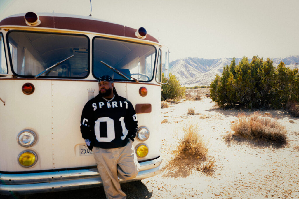 A photo of Xavier Omar standing in front of a bus in a mountainous area