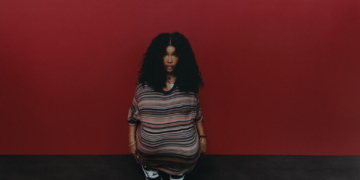 A photo of SZA wearing Vans against a red wall