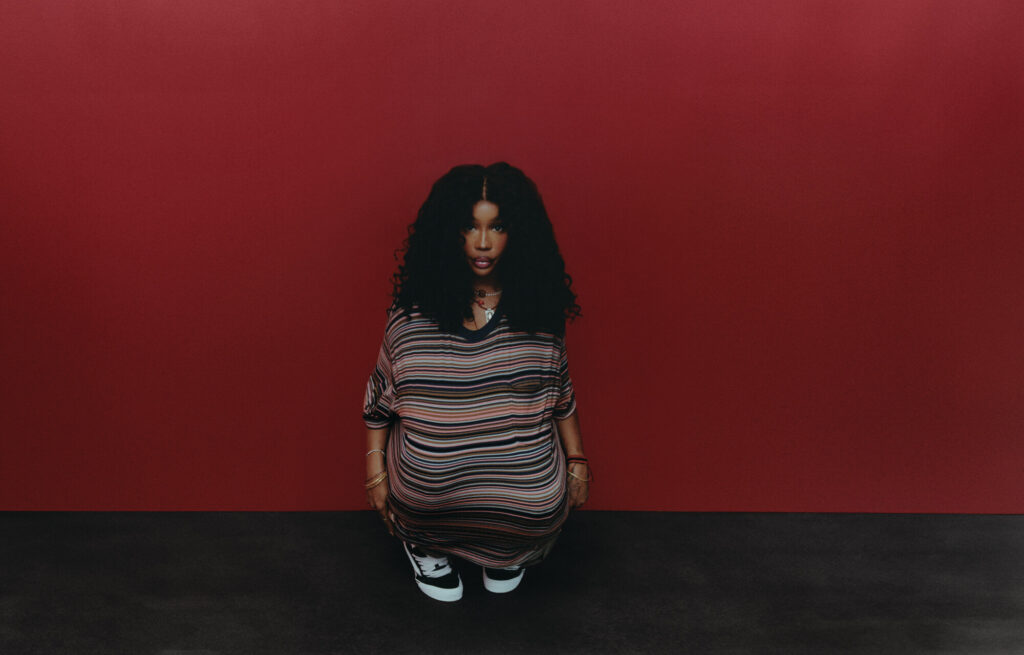 A photo of SZA wearing Vans against a red wall