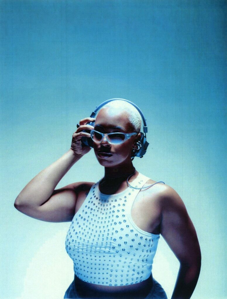 A photo of Zyah Belle with headphones against a blue backdrop