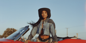 India Shawn in a red car wearing a denim western jacket and hat