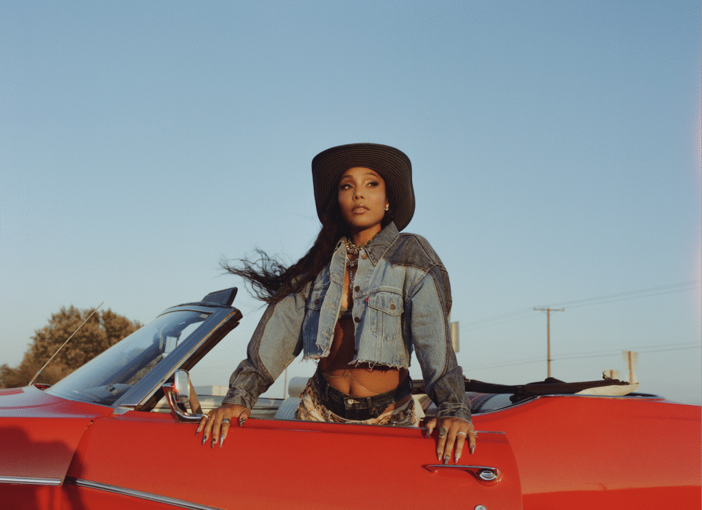 India Shawn in a red car wearing a denim western jacket and hat