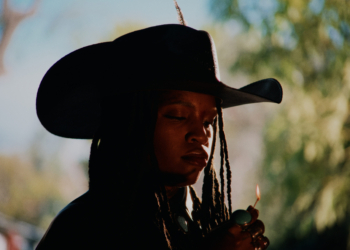 A photo of singer Ambré wearing a cowboy hat and lighting a lighter