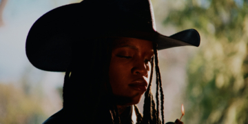 A photo of singer Ambré wearing a cowboy hat and lighting a lighter