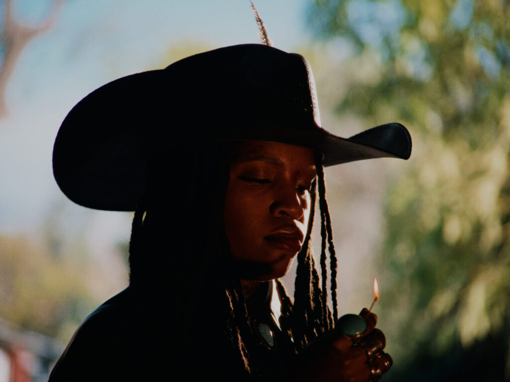 A photo of singer Ambré wearing a cowboy hat and lighting a lighter