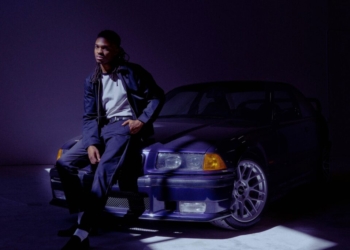 A photo of singer Tone Stith leaning against a car, looking into the camera