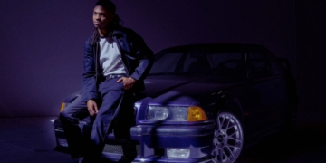 A photo of singer Tone Stith leaning against a car, looking into the camera